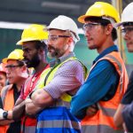 Builders of different ethnicity's in hard hats and hi vis standing next to each other in a line