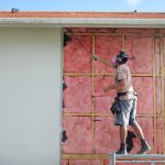 Man in PPE checking the wall panels of a home for asbestos particles