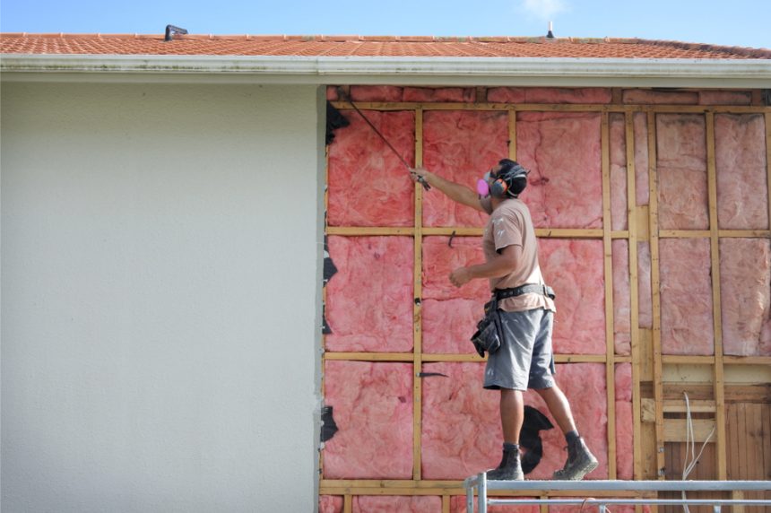 Man in PPE checking the wall panels of a home for asbestos particles