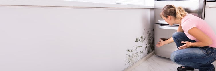 A woman looks at mould in a house.