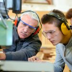 Apprentices watch construction mentor use machine on work site