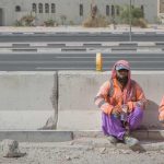 migrant construction workers sitting down on side of construction site wearing PPE