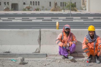 migrant construction workers sitting down on side of construction site wearing PPE