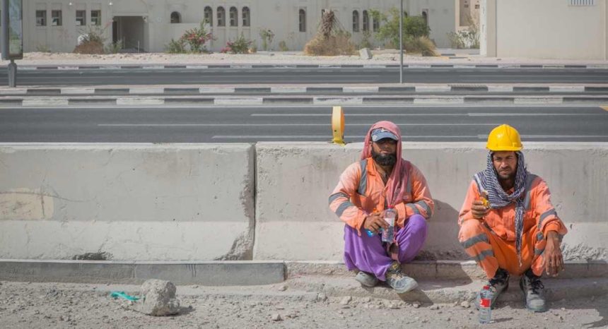 migrant construction workers sitting down on side of construction site wearing PPE