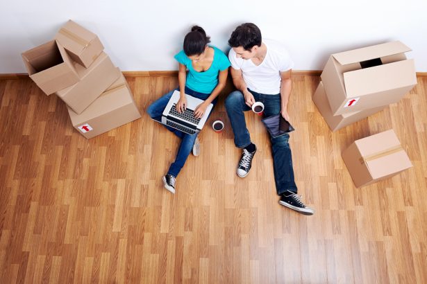 Millenials sitting on home floor surrounded by moving boxes