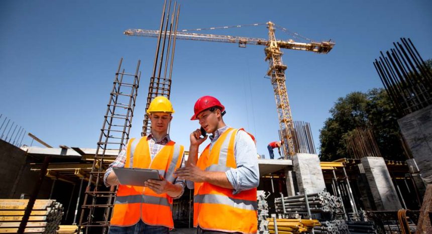 Engineers on worksite looking over tablet in front of crane