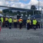 Concrete trucks and traides in high vis ppe blocked behind fence by union members