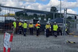 Concrete trucks and traides in high vis ppe blocked behind fence by union members