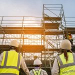 Safety officers in high vis protective equipment looking up at scaffolding on construction site