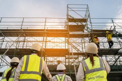 Safety officers in high vis protective equipment looking up at scaffolding on construction site