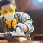 Women wearing safety glasses and noise cancelling headphones plaining wood on a machine