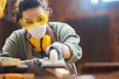 Women wearing safety glasses and noise cancelling headphones plaining wood on a machine