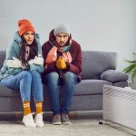 Couple in winter clothes huddled up on couch in Australian home