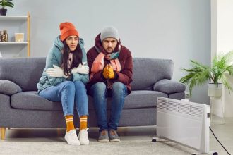 Couple in winter clothes huddled up on couch in Australian home