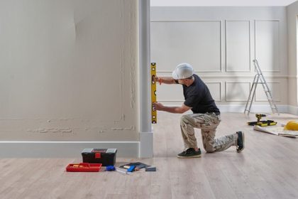 Repair man in hardhat holding level onto a wall in a home