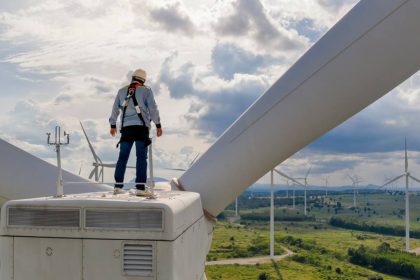 Tradie in harness standing atop windmill in wind farm