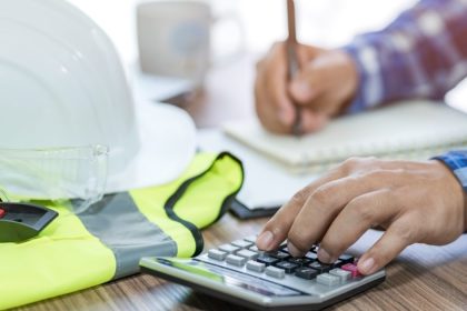 Man writing his tax return on desk with construction hard hat and vest on table