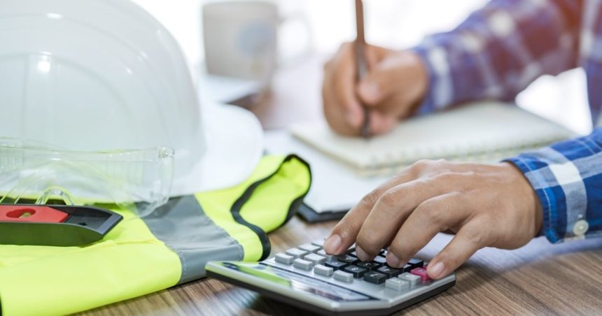 Man writing his tax return on desk with construction hard hat and vest on table