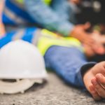 tradie lying on the concrete after a fall while man tries to revive him