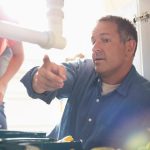 Plumber under sink pointing in front of customer