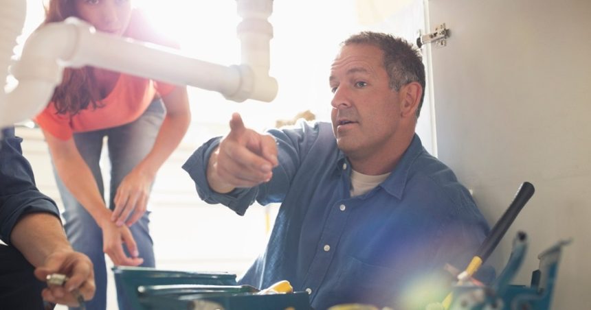 Plumber under sink pointing in front of customer