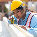 woman in hardhat measuring timber on construction site