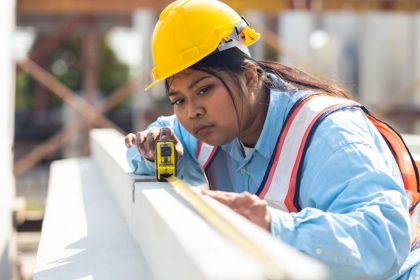 woman in hardhat measuring timber on construction site