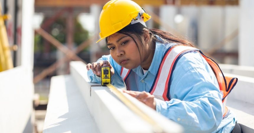 woman in hardhat measuring timber on construction site