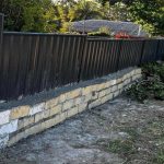 a badly built wall with a fence balanced on top