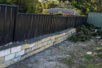 a badly built wall with a fence balanced on top