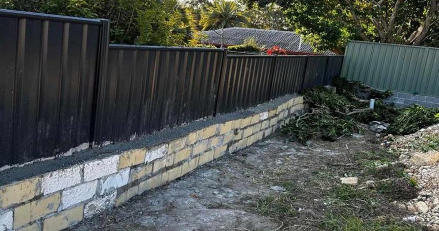 a badly built wall with a fence balanced on top