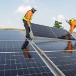 Two workers installing solar panels on rooftop