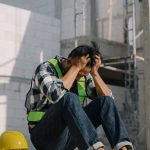 Financially stressed construction worker sitting down on site