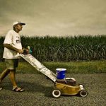 claude harvey pushes his lawnmower past cane fields