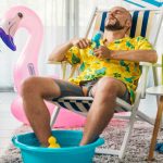 a man feels hot inside his home and attempts to cool down using a fan and paddling pool