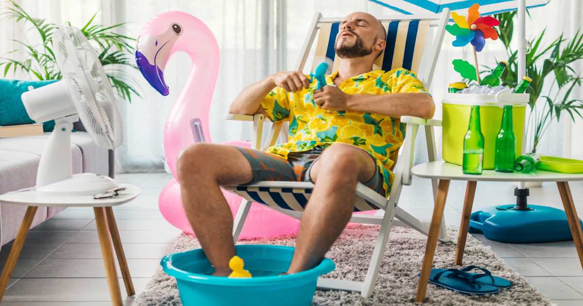 a man feels hot inside his home and attempts to cool down using a fan and paddling pool