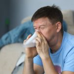 man sneezing into tissue at home