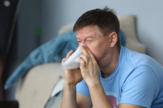 man sneezing into tissue at home