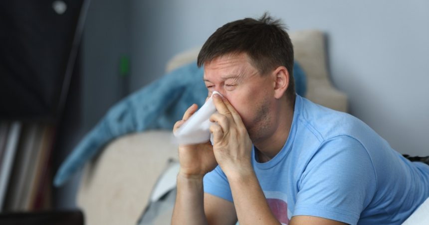 man sneezing into tissue at home