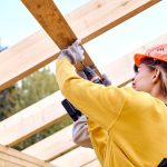 woman drilling into wood in construction gear on a worksite