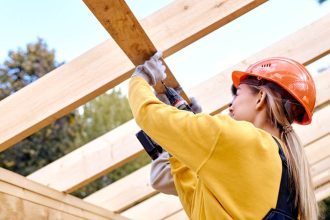 woman drilling into wood in construction gear on a worksite