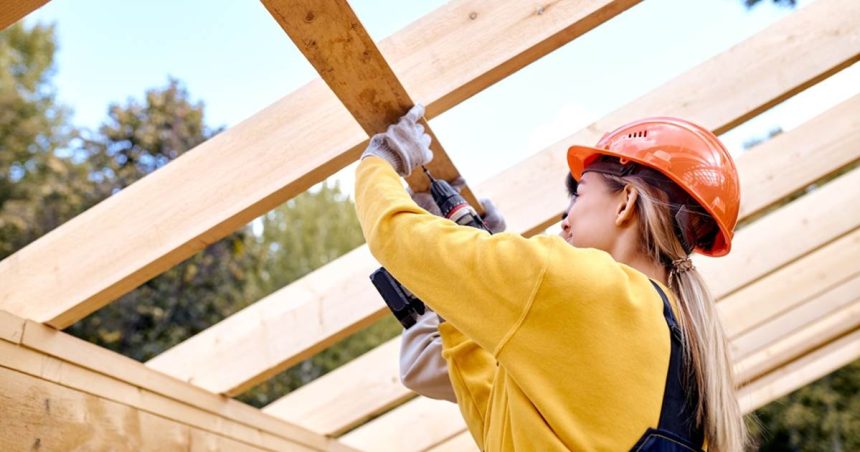 woman drilling into wood in construction gear on a worksite